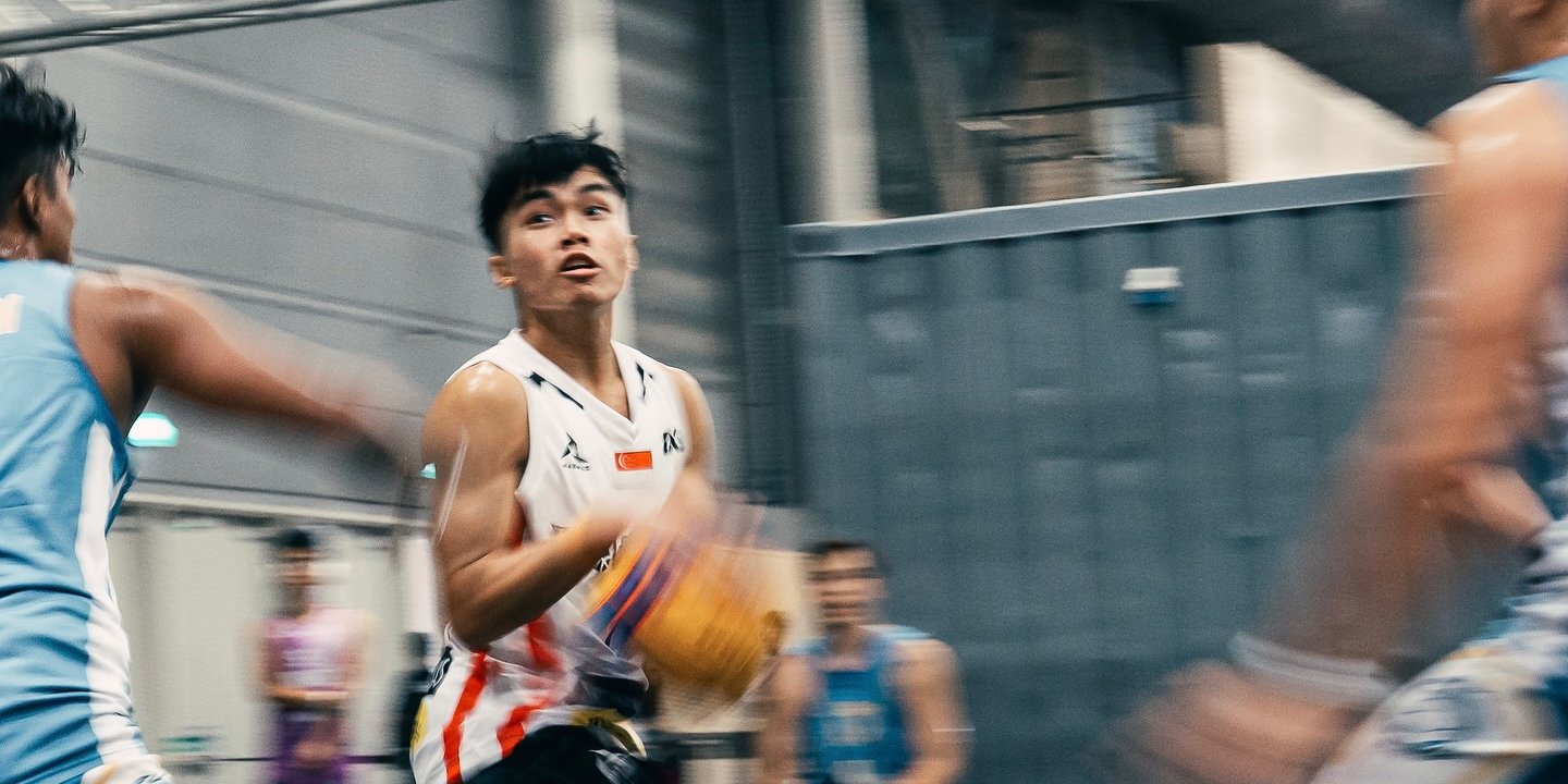 A 3x3 Wolfgang SG player in the white kit carrying the ball upcourt, the game blurred around him